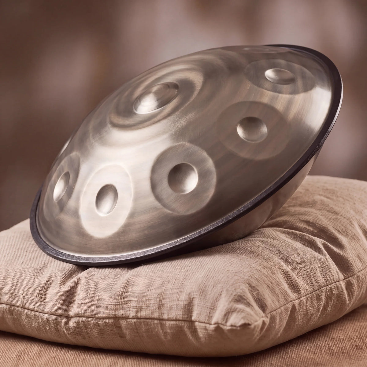 Handpan D Kurd 12 notes Nautile Kovapan acier satiné – posé de profil sur coussin lin fond bokeh