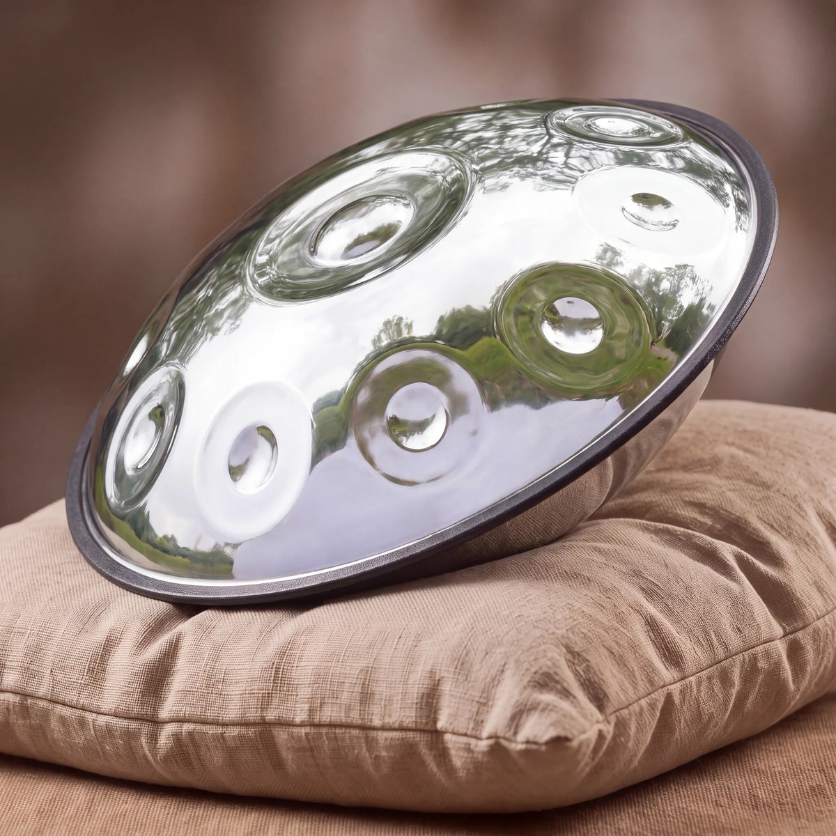 Handpan D Kurd 9 notes SELENE argenté poli miroir Kovapan – posé de profil sur coussin lin fond bokeh