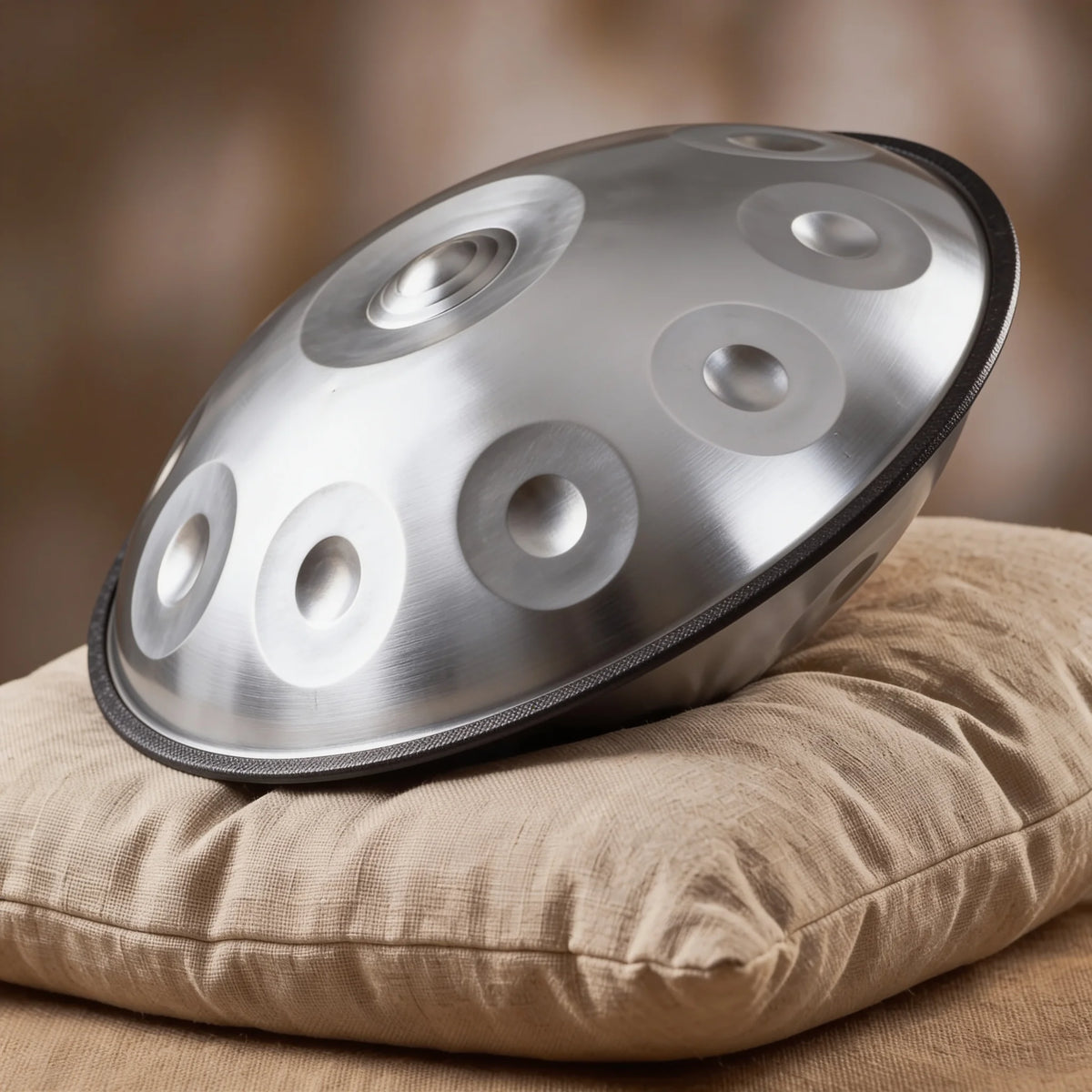 Handpan STELLAR argenté posé de profil sur un coussin en lin – Kovapan