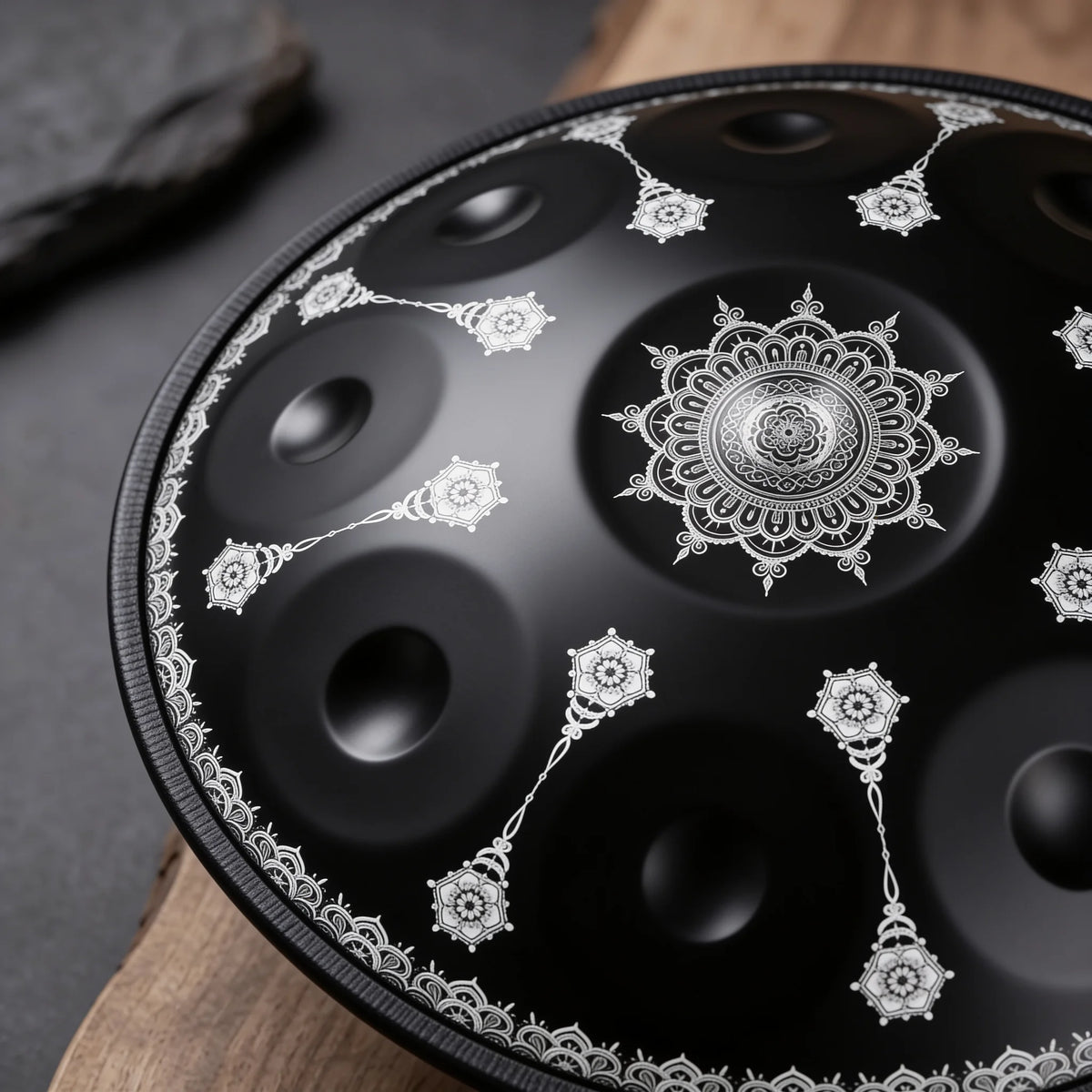 Gros plan du handpan pas cher OBSIDIENNE noir mat en Ré mineur Kurd, mandala central et motifs argentés, posé sur bois et ardoise – Kovapan