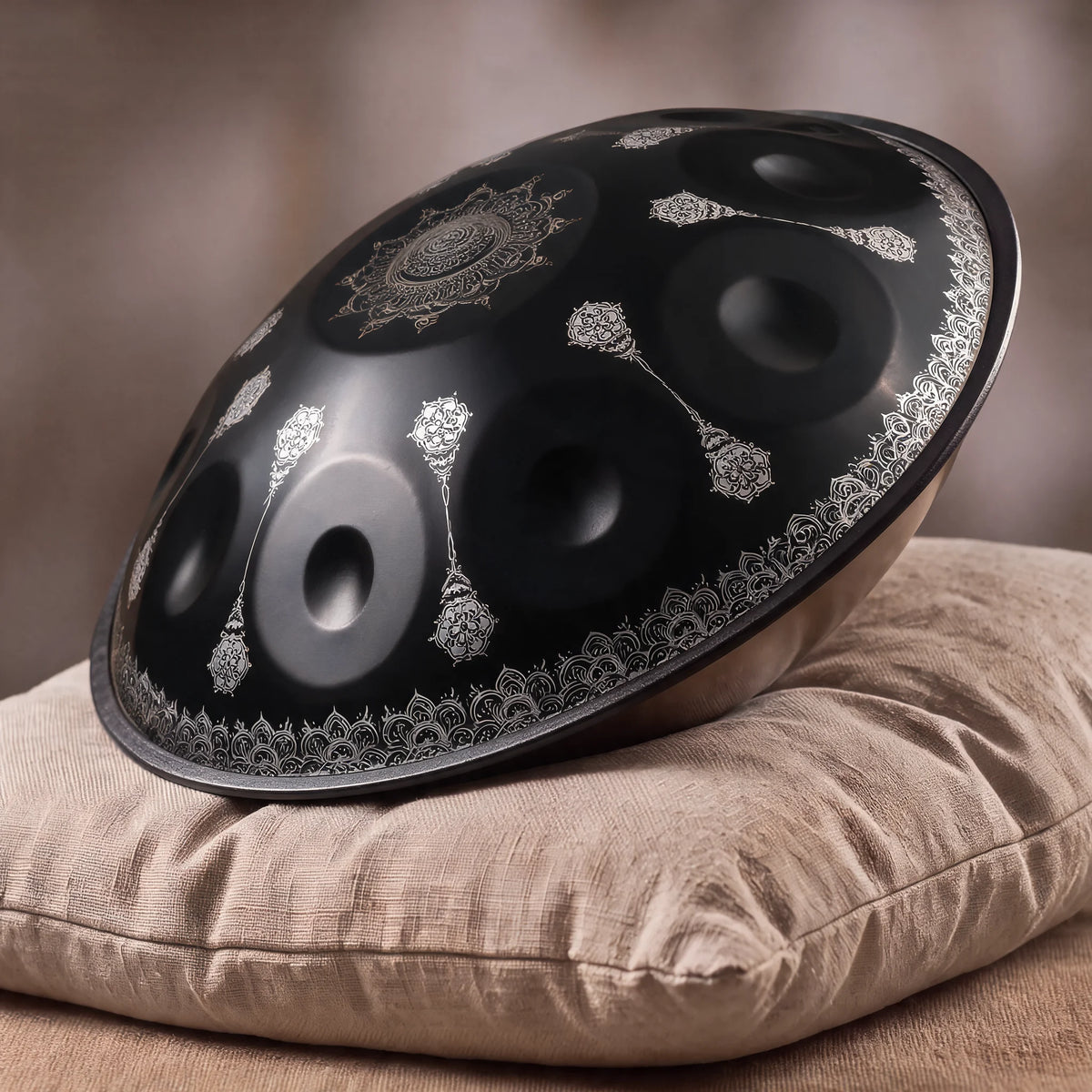 Handpan pas cher OBSIDIENNE noir mat posé de profil sur un coussin en lin, décors mandala argentés sur la coque – Kovapan