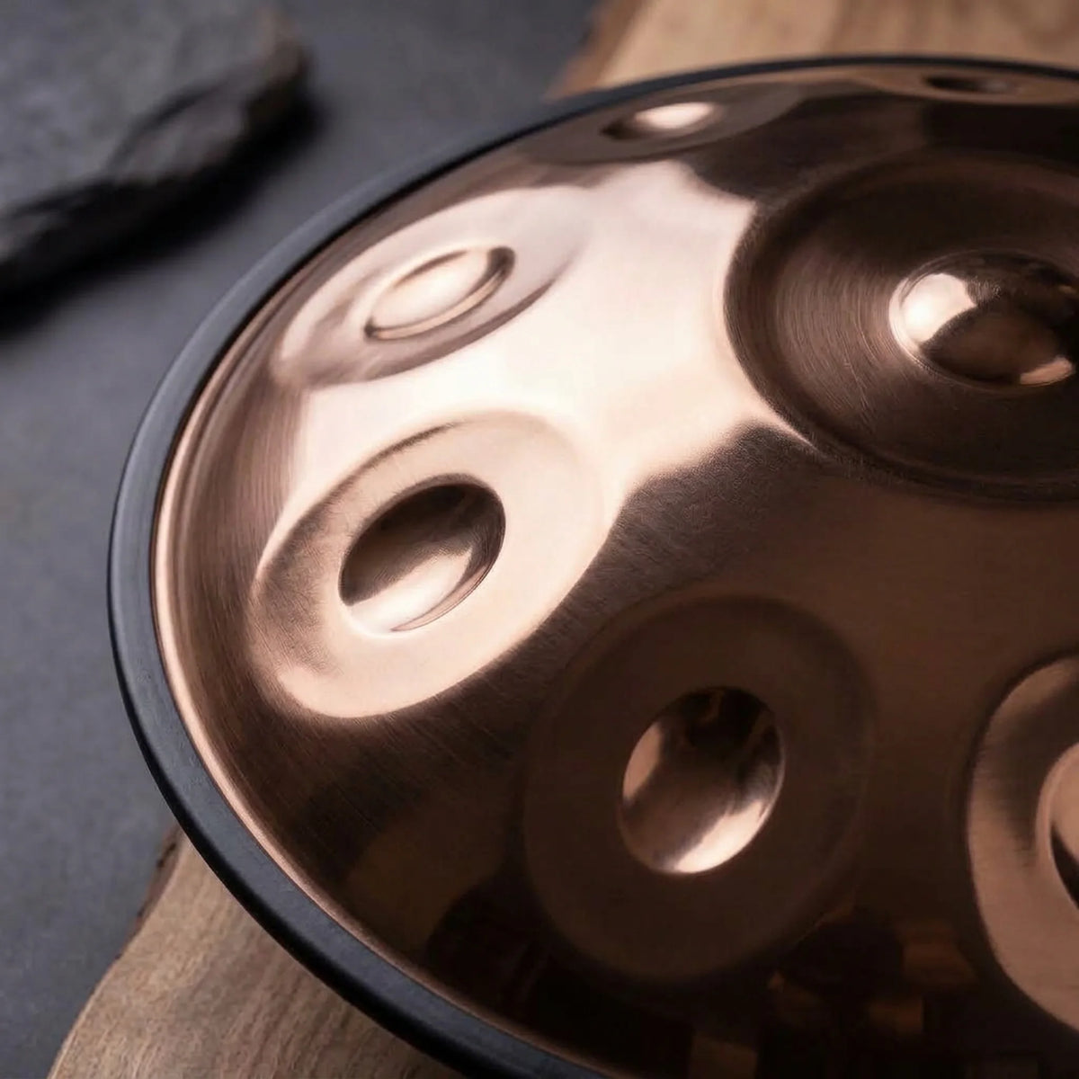 Handpan percussion D Kurd bronze poli – gros plan champs de notes reflets chauds sur bois et ardoise – Kovapan