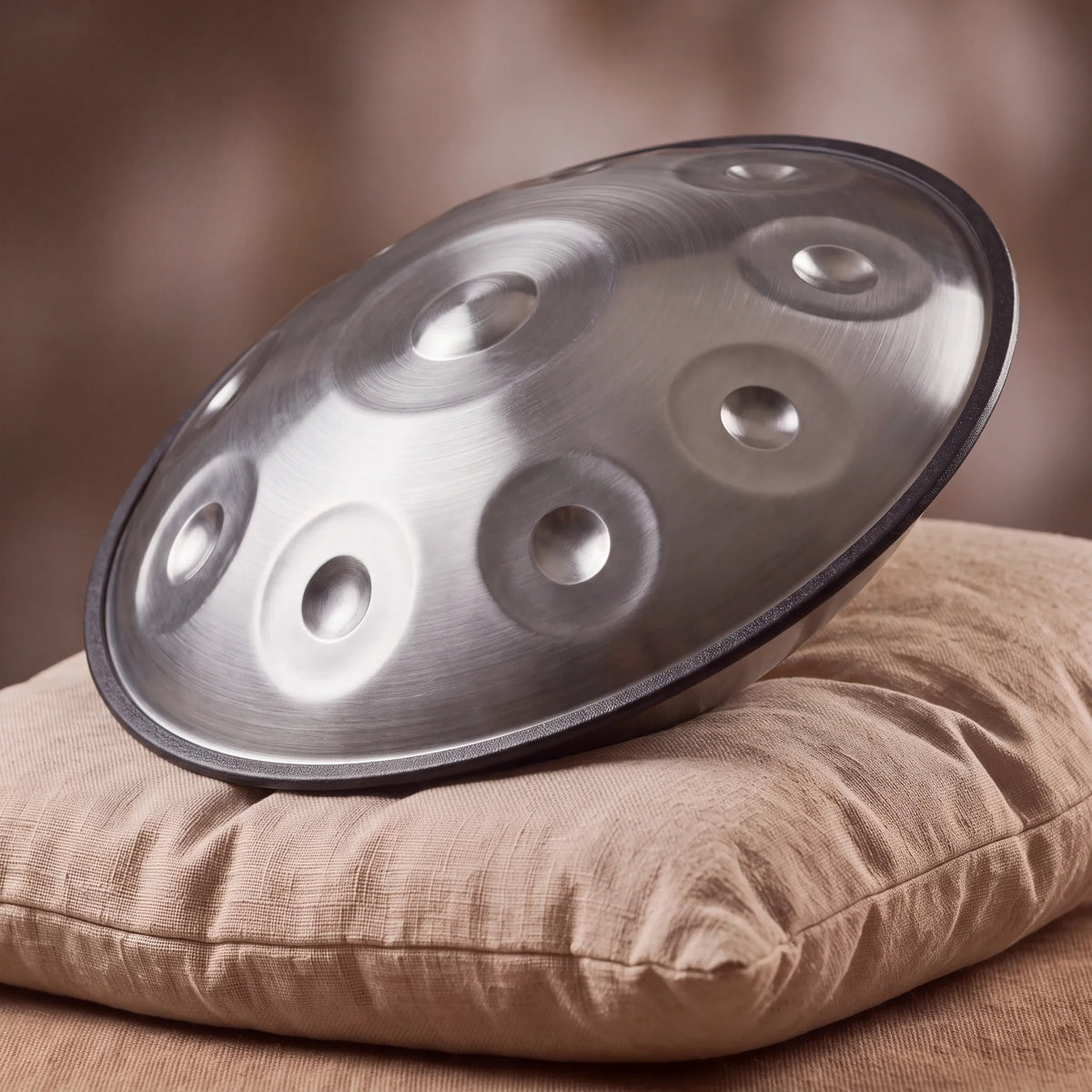 Handpan Sol mineur Kovapan acier brossé – posé de profil sur coussin lin fond bokeh chaud