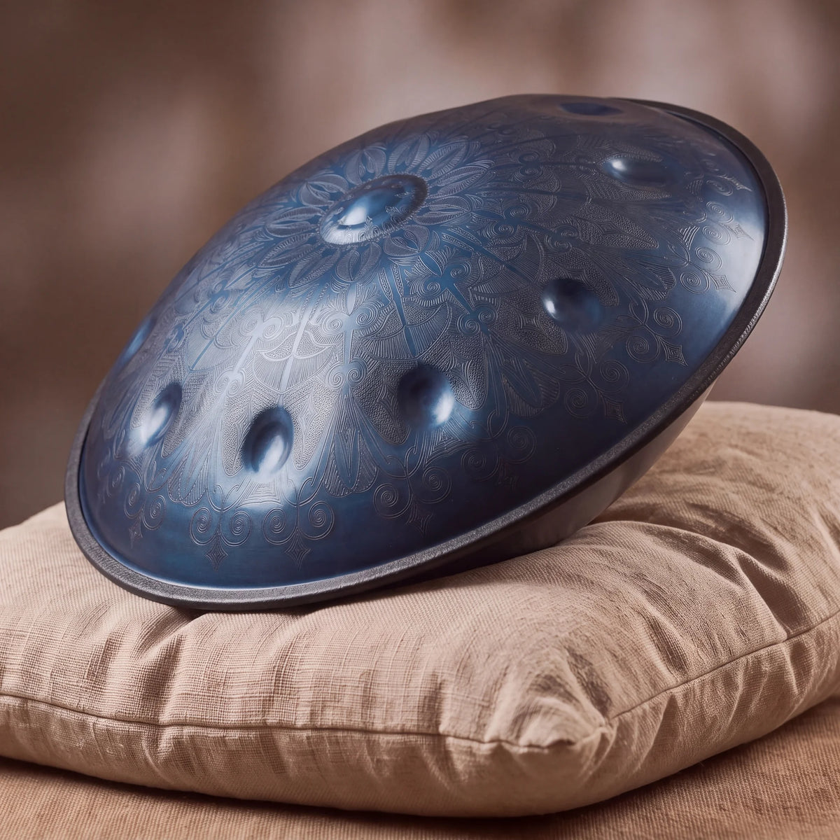 Handpan bleu Abyss Kovapan – posé de profil sur coussin lin fond bokeh chaud