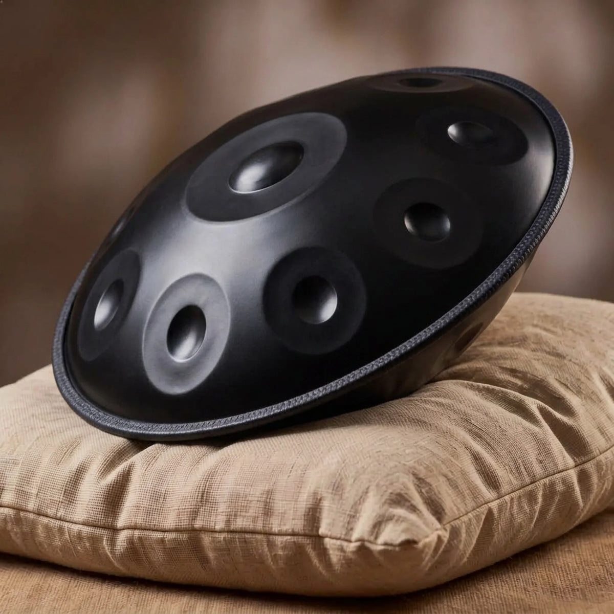 Handpan D Kurd 432 Hz noir mat Kovapan – posé de profil sur coussin lin fond bokeh chaud
