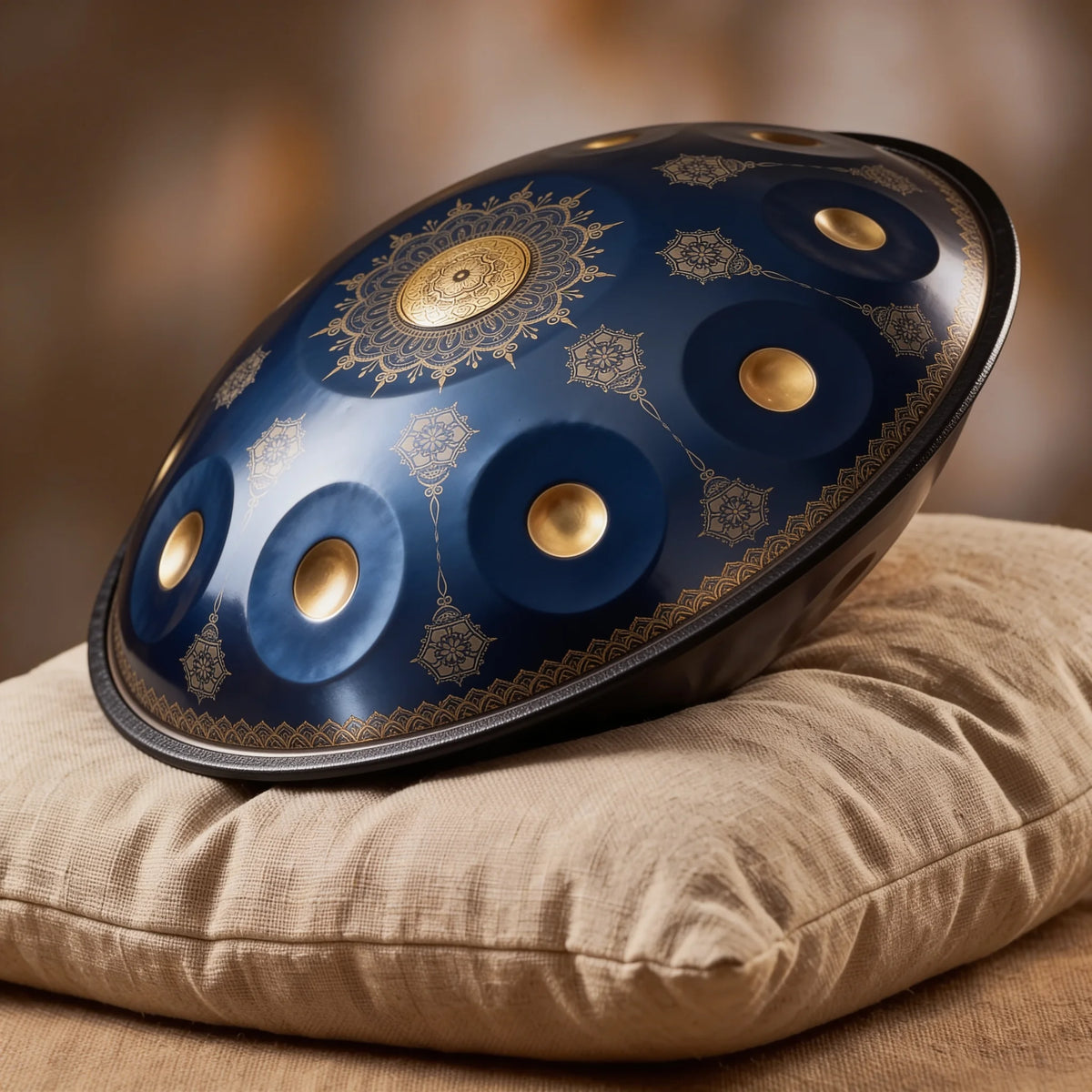 Handpan Mandala Kovapan bleu nuit, motifs dorés – posé de profil sur coussin lin fond bokeh