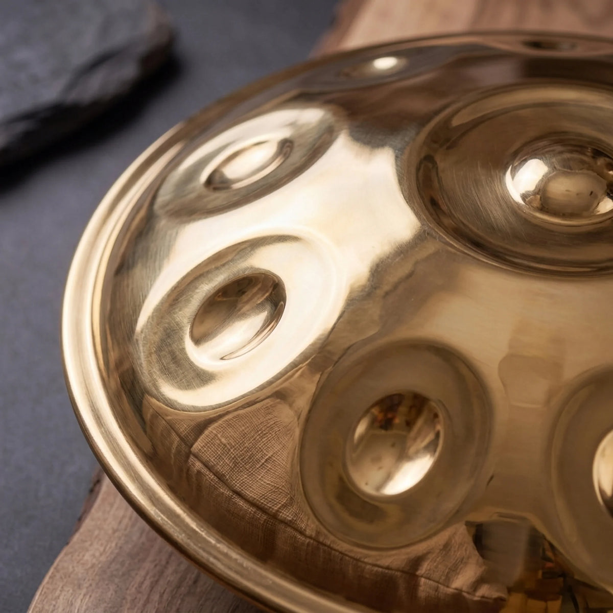 Handpan instrument de musique doré poli – gros plan champs de notes reflets chauds sur bois et ardoise – Kovapan
