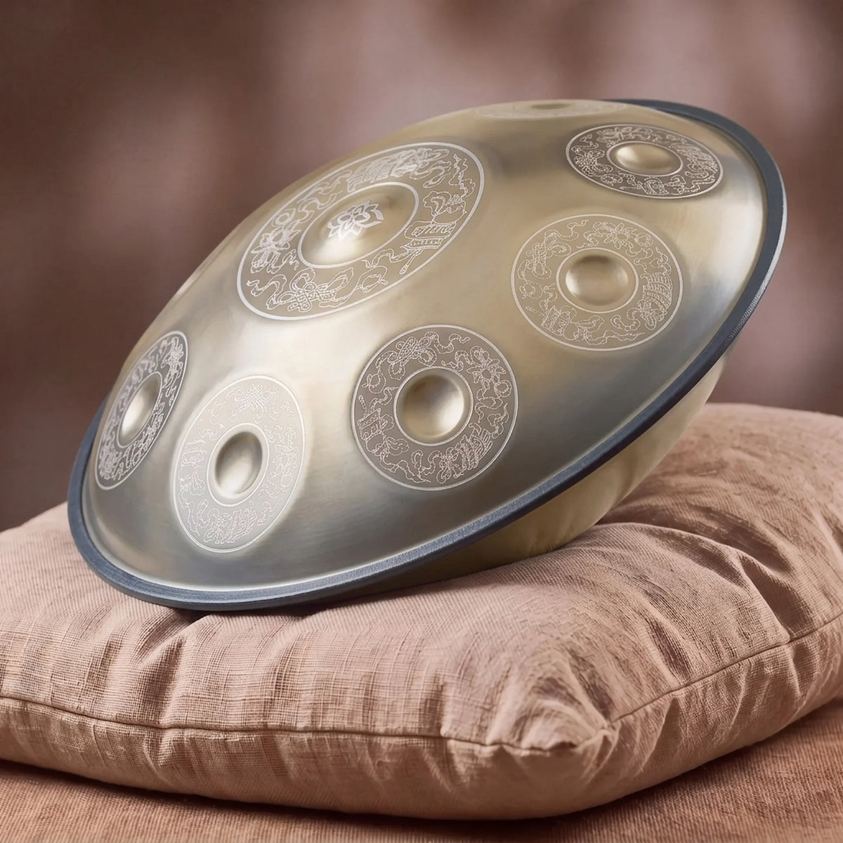 Handpan professionnel vermeil gravures orientales – posé de profil sur coussin lin fond bokeh chaud – Kovapan