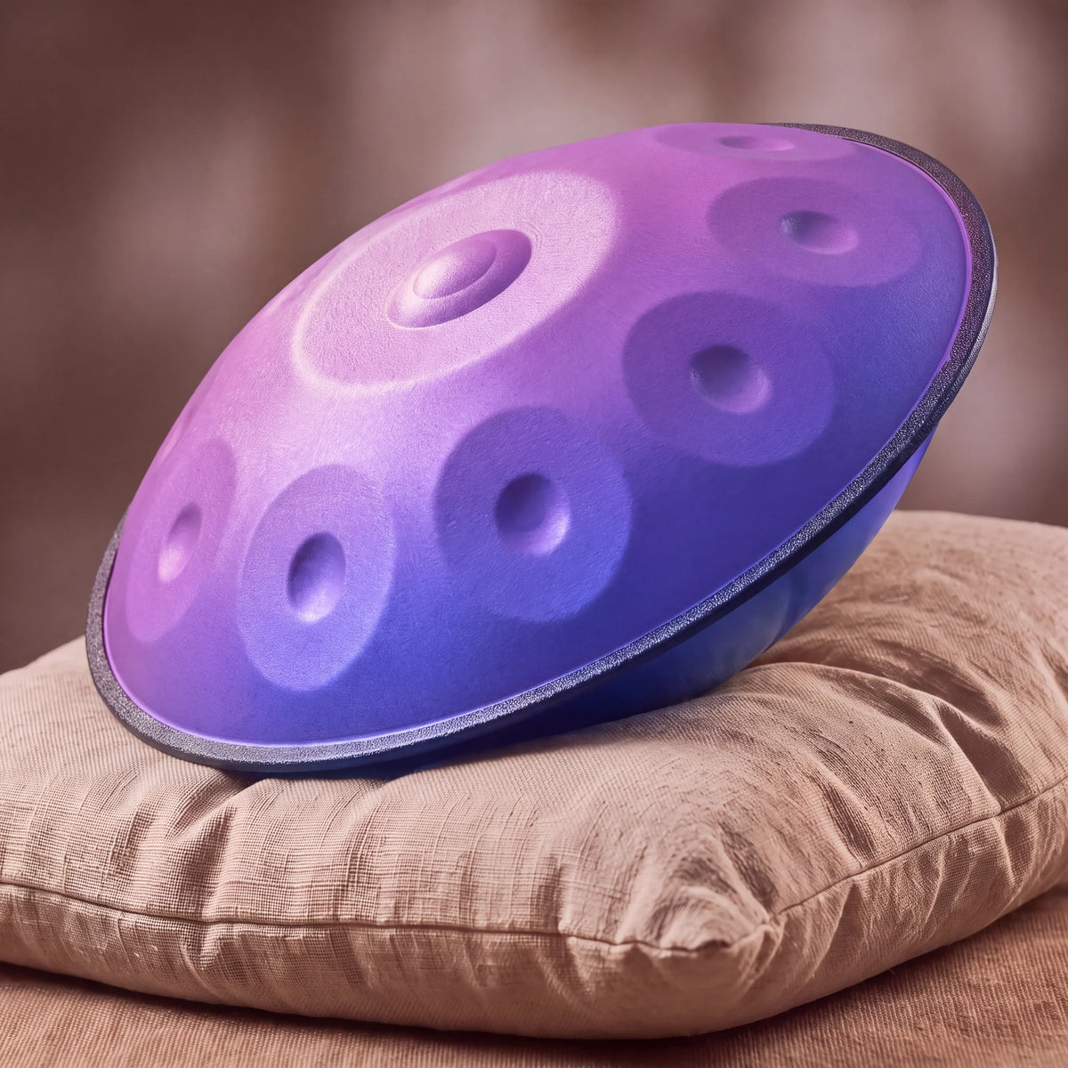 Handpan violet iris dégradé rose-violet Kovapan – posé de profil sur coussin lin fond bokeh chaud