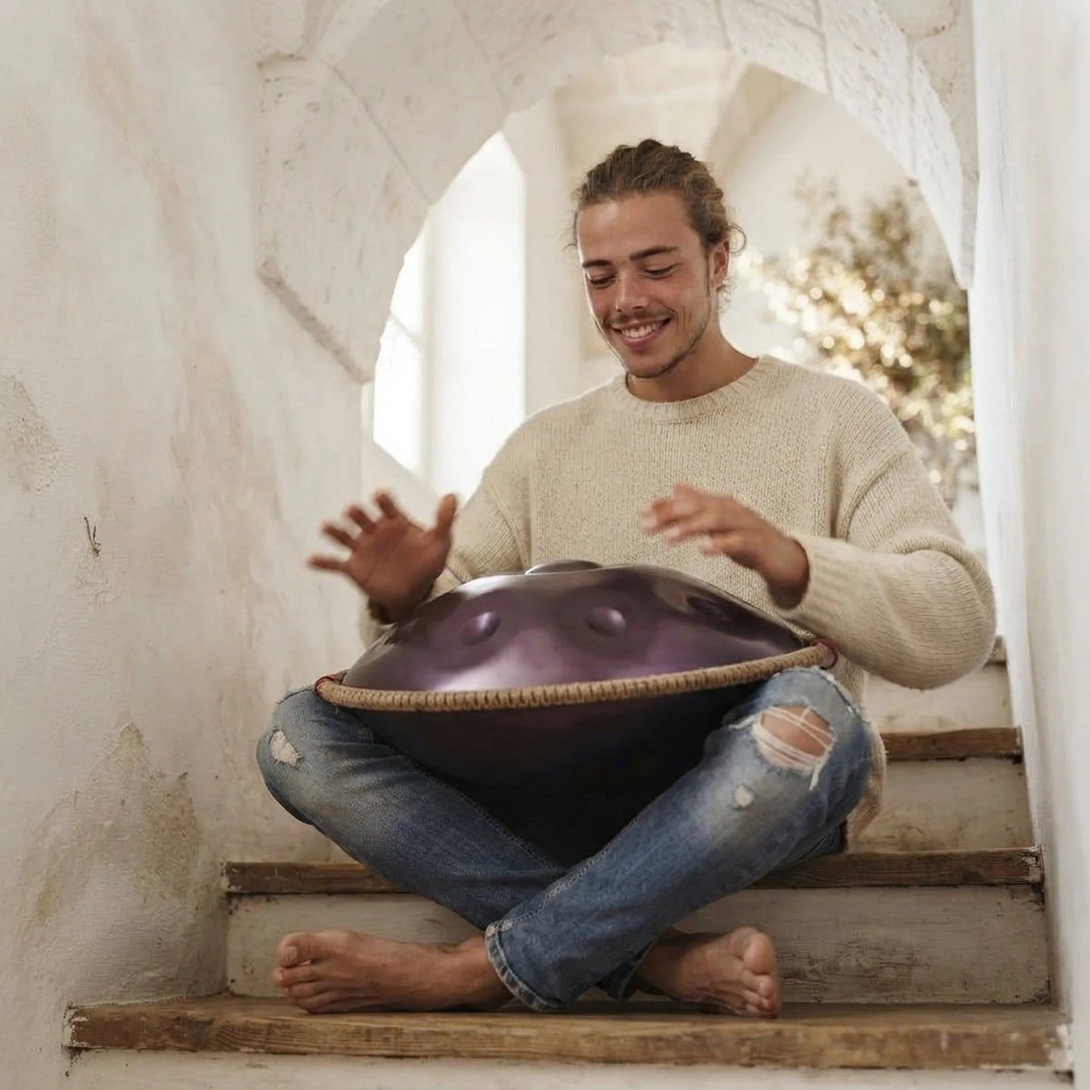 Handpan 12 notes D Kurd violet – musicien souriant jouant assis dans escalier sous arche – Kovapan