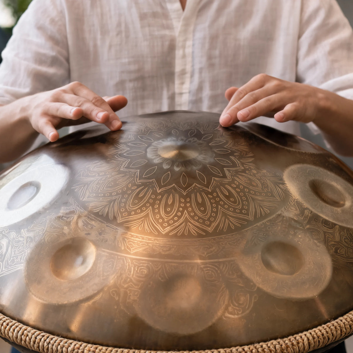 Mains jouant du tambour handpan DUNE doré gravé d'un mandala, bord tressé naturel, en gros plan – Kovapan
